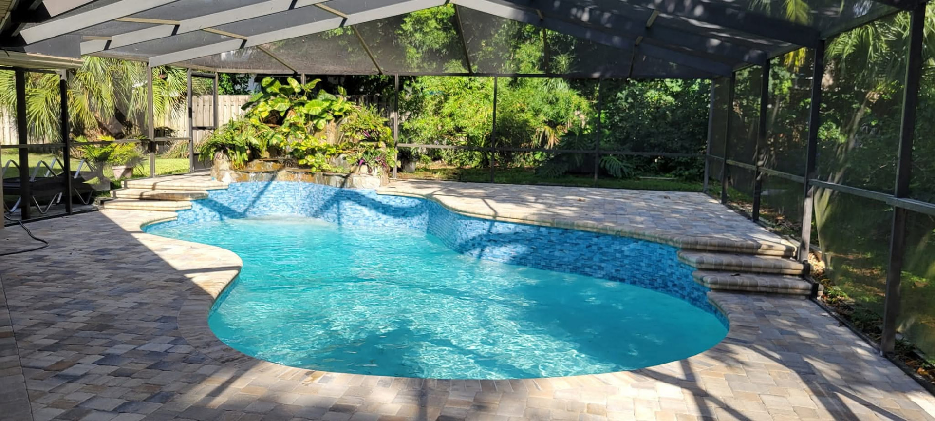 Lagoon style pool with rock waterfall and paver deck under a screen enclosure